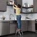 A woman standing on a Cosco black and platinum step stool in a kitchen.