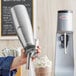 A person using a Chef Master stainless steel whipped cream dispenser to make a milkshake.
