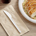 A plate of food with a white EcoChoice compostable plastic knife on a napkin on a table.