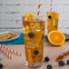 A Libbey stackable Tritan plastic beverage glass of iced tea with oranges and blueberries on a table.