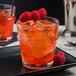 A Libbey Tritan plastic double rocks glass filled with orange drink, ice, and raspberries.