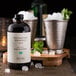 A bottle of Woodford Reserve Mint Julep Simple Syrup on a table with ice and mint.