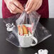 A person holding a cup of hot chocolate with marshmallows and candy in a plastic bag.