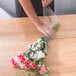A person wrapping a bouquet of flowers in LK Packaging clear plastic deli wrap.
