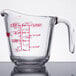 An Anchor Hocking clear glass measuring cup with red writing on it.