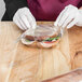 A gloved hand putting a sandwich in a plastic bag.