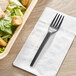 A black EcoChoice CPLA plastic fork on a white napkin next to a salad.