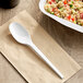 A white EcoChoice CPLA plastic spoon on a napkin with a bowl of food.