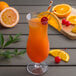 A Libbey Tritan plastic hurricane glass filled with orange juice and fruit.