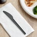 A EcoChoice black plastic knife on a napkin next to a plate of food.