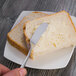A hand using a Oneida Baguette stainless steel butter spreader to spread butter on a piece of bread.