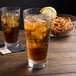Two Arcoroc Urbane stackable cooler glasses with ice tea and a bowl of pretzels on a table.