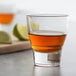 An Arcoroc shot glass with brown liquid and limes.