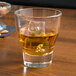 An Arcoroc stackable old fashioned glass filled with ice and whiskey on a table.