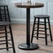 A Lancaster Table & Seating black cast iron counter height table base pole on a table with two stools.