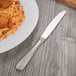 A plate of spaghetti and meatballs with a Oneida Baguette stainless steel table knife on a wooden table.