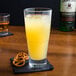 A stack of Arcoroc Urbane cooler glasses filled with yellow liquid next to pretzels.