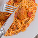 A Oneida Baguette stainless steel dinner knife and fork on a plate of spaghetti and meatballs.