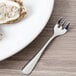 A Oneida Baguette stainless steel oyster fork on a white plate with oysters.