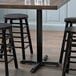 A Lancaster Table & Seating black cast iron counter height table base with three stools around it.