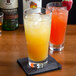 A stack of Arcoroc highball glasses filled with orange and yellow liquid on a table with ice.