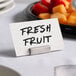 An American Metalcraft stainless steel square rod table card holder with a place card on a table with fresh fruit.