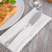 A Oneida Baguette stainless steel fish knife on a napkin next to a plate of food.