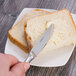 A hand spreading butter on a piece of bread with a Oneida Baguette stainless steel butter knife.