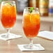 Two Acopa stemmed iced tea glasses filled with orange liquid, lemons, and mint leaves.