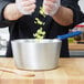 A person using a Vollrath Wear-Ever sauce pan with a blue silicone handle to cook celery.