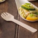 A wooden taster fork next to a spoonful of pasta with vegetables.