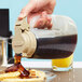 A person pouring syrup from a Tablecraft Dispenser Jar onto a waffle.