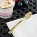 A Fineline gold plastic tasting spoon with a glass of dessert.