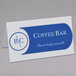 A close-up of a white scored C-Line tent card on a counter with a sign that says coffee bar.
