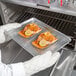 A person in gloves holding a Choice half size aluminum sheet pan with salmon on it.