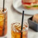 A glass of iced tea with an EcoChoice black paper straw and a sandwich on a table.
