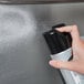 A person using Weiman Stainless Steel Cleaner & Polish spray on a stainless steel sink.