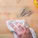 A hand wiping a wooden table with a white towel using Goo Gone Pro-Power Adhesive Remover Spray Gel.