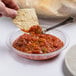 A hand holding a tortilla chip and dipping it into a Cambro pebbled bowl of salsa.