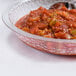 A Cambro pebbled serving bowl filled with red sauce on a table with a spoon.
