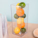 A Cal-Mil clear acrylic square accent vase with lemons, limes, and oranges inside.