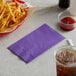 A basket of french fries and a purple napkin next to a drink.