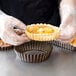 A person in gloves placing a pastry in a Gobel fluted deep tart pan.