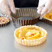 A person preparing a tart in a fluted tart pan with a removable bottom.