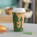 A table with a coffee cup in a Kraft paper cup with a green lid and a croissant.