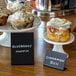 A table with a plate of muffins and a black American Metalcraft chalkboard sign with white text on it.