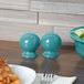 A wood table with a bowl of salad, Fiesta turquoise salt shaker, and bowl.