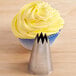 A cupcake with yellow frosting next to a metal cone with an open star tip.