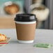 A Choice white paper hot cup with a black lid and a croissant on a table.