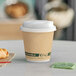 A EcoChoice 8 oz. sleeveless paper hot cup with a lid next to a croissant on a table.